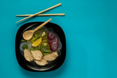Siyah tabak Vietnamlı Pho çorbası ve mavi arka planda tavuk..