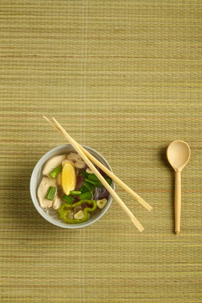 Un plato ligero de sopa Pho vietnamita con pollo en una esterilla y palillos y una cuchara — Foto de Stock