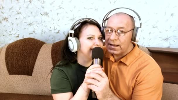 Man and woman family at home on the couch with headphones singing in a karaoke microphone — Stock Video