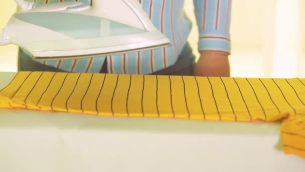 Ett järn i en kvinnlig hand slätar ut färgade kläder på en strykbräda — Stockvideo