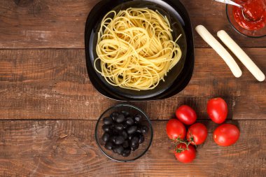 Kadın eli, ahşap bir masada siyah bir tabakta spagetti sosu sürüyor..