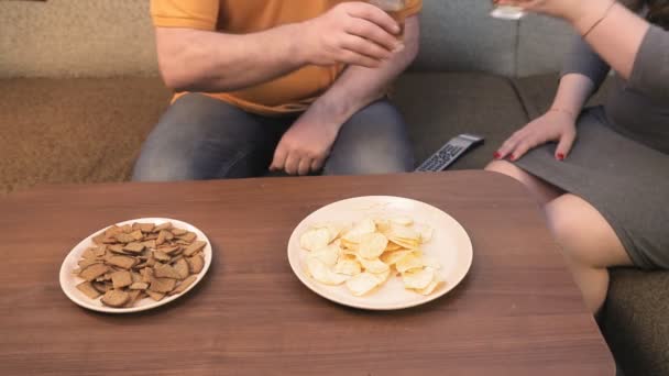Чоловік і жінка на дивані п'ють пиво і дивиться телевізор без облич — стокове відео