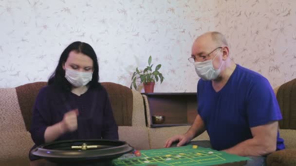 의료용 마스크를 쓰고 있는 남편 과 아내는 코로나 바이러스 예방을 위해 격리 된 채 집에서 룰렛을 한다. — 비디오