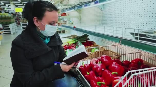 La compradora en una máscara protectora en una tienda elige verduras durante el período de cuarentena. Movimiento lento . — Vídeo de stock