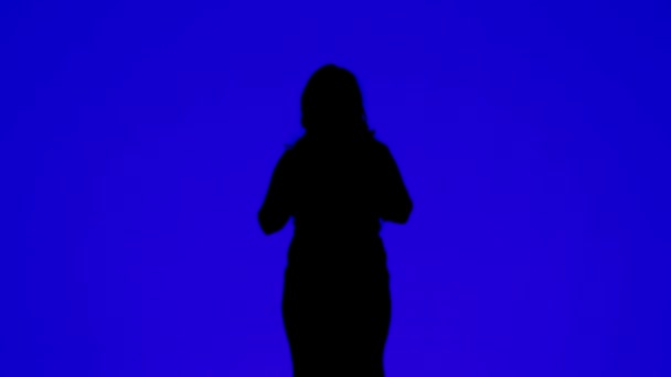 Silueta de una mujer delgada con auriculares y bailando con la música sobre un fondo azul . — Vídeos de Stock