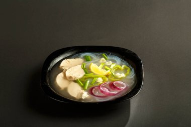 Siyah arka planda tavuklu bir tabak Vietnam Pho çorbası.