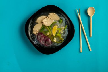 Siyah tabak Vietnamlı Pho çorbası ve mavi arka planda tavuk..