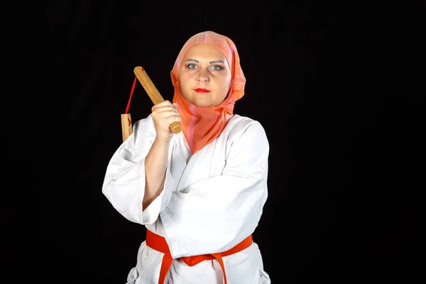 Muslim woman in kimono and hijab in karate class is training with nunchucks