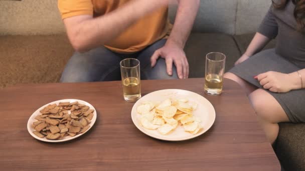 Чоловік і жінка на дивані п'ють пиво і попросять телевізор . — стокове відео