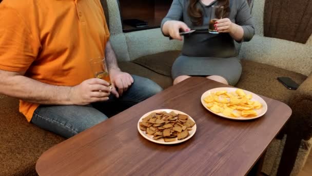 Marido y esposa en casa en el sofá discuten sobre la televisión qué ver y beber cerveza sin rostros . — Vídeos de Stock