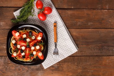 Çeri domatesli zeytin ve keten peçeteli mozzarella ile süslenmiş soslu siyah bir tabak. Yer ayır.