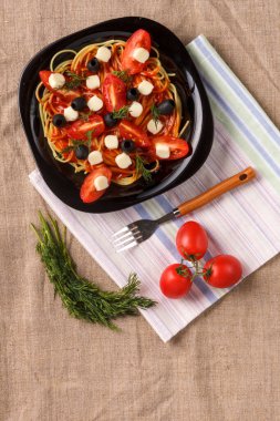 Çeri domatesli zeytin ve keten peçeteli mozzarella ile süslenmiş soslu siyah bir tabak. Yer ayır.