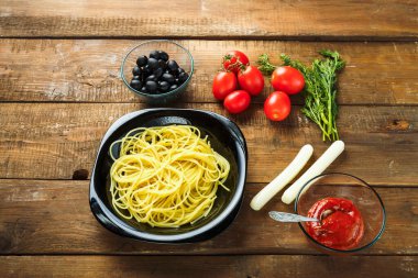 İtalyan yemeklerini ahşap bir masada süslemek için makarna ve sebzeli siyah tabak..