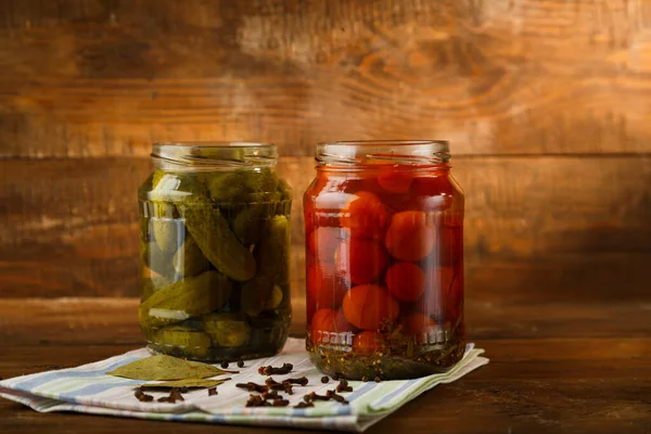 Burkar med inlagda hemmagjorda pickles och körsbärstomater och strödda kryddor på en linnehandduk på ett träbord. — Stockfoto