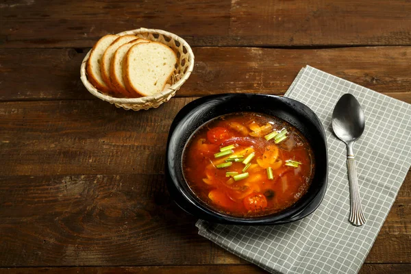 Черное блюдо итальянского томатного супа с картошкой и грибами на деревянном столе на салфетке и ложке с хлебом . — стоковое фото