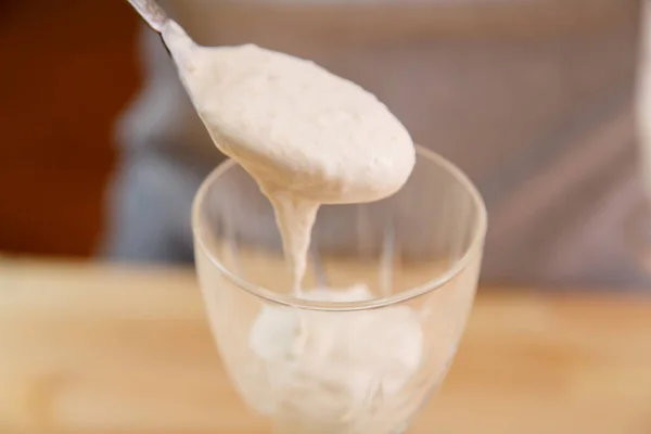 Uma mão feminina segura uma colher e coloca a massa esmagada de banana com sorvete em um copo de smoothie . — Fotografia de Stock