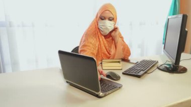 Karantina döneminde tıbbi maske takmış Müslüman bir kadın ofiste aletlerle çalışıyor..