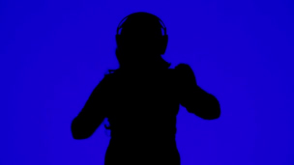 Silhueta de uma mulher em fones de ouvido e dançando a música em um fundo azul — Vídeo de Stock