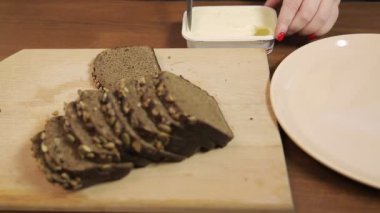 Bir kadın eli, bıçak kullanarak çavdar ekmeğini krem peynirle yayar..