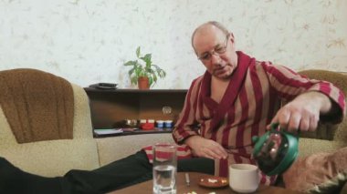 Evdeki kanepede bornozlu bir adam grip benzeri semptomlarla güçlü bir çay içiyor.