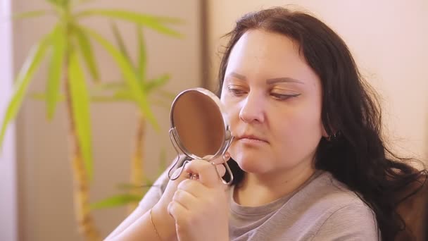 Une jeune femme pince les poils du visage à l'aide de pinces devant un miroir à la maison — Video