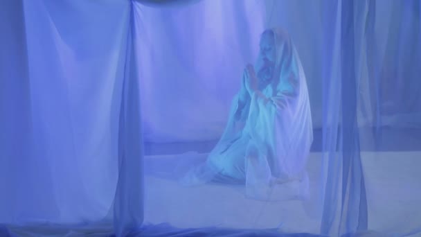 Uma jovem muçulmana de branco faz uma oração antes do casamento atrás de uma cortina branca — Vídeo de Stock