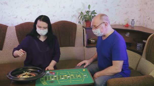 Una pareja casada con máscaras médicas juega a la ruleta en casa en cuarentena para la prevención del coronavirus — Vídeo de stock