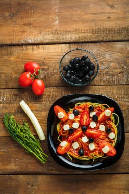 Çeri domatesli ve ahşap masadaki mozzarella soslu siyah tabak..