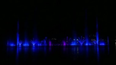 Suyun üzerinde çok renkli çeşmelerin gece gösterisi suya yansıyor.