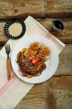 Sebzeli soba karabuğday eriştesi ve keten peçetede beyaz bir tabakta tavuk pirzolası..