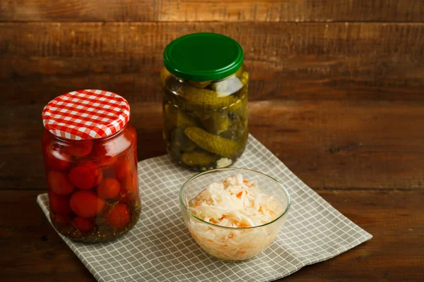 Burkar med inlagda tomater och gurkor med hemlagad pickles och surkål på ett träbord. — Stockfoto