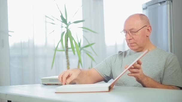 Un hombre está considerando un álbum familiar con fotos en casa . — Vídeos de Stock