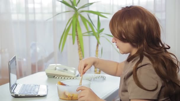 A woman at work in the office during lunch break has lunch using Chinese chopsticks and speaks on the phone — Stock Video