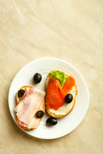 Blandade smörgåsar med fiskbacon och grönsaker på ett ljust bord på en tallrik. — Stockfoto