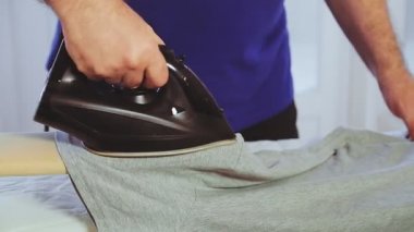 Bir adamın elindeki ütü ütü masasındaki giysileri ütülemektir..