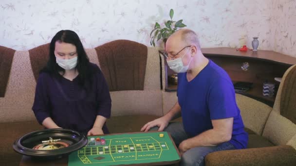 Ein Ehepaar in medizinischen Masken spielt zu Hause Roulette in Quarantäne in Isolation zur Verhinderung von Coronavirus. — Stockvideo