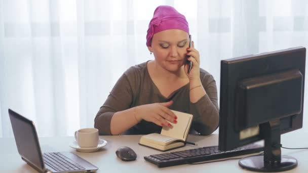 Uma mulher judia em uma cobertura para a cabeça em um escritório trabalha em um computador e fala ao telefone — Vídeo de Stock