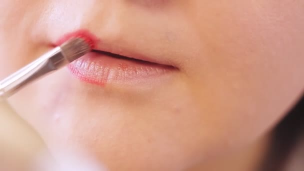 Een jonge vrouw brengt rode lippenstift aan op haar halve lip met een kwast voor een spiegel — Stockvideo