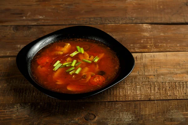 Plato negro de sopa de tomate italiano con patatas y champiñones sobre una mesa de madera . —  Fotos de Stock