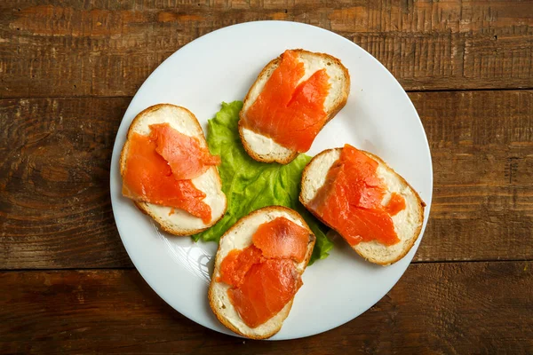 Bruschettas med lax och färskost på en vit platta på ett träbord. — Stockfoto