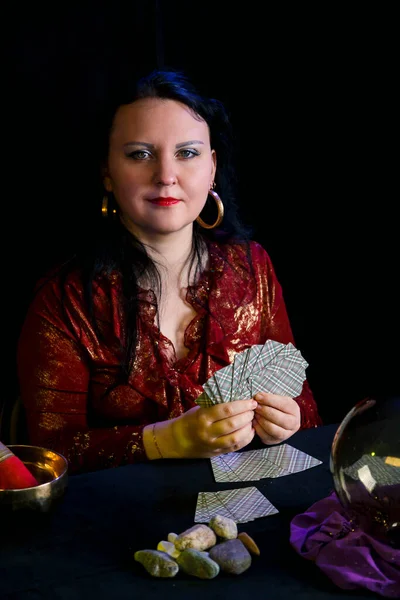 A young soothsayer in a magic salon with cards in her hands on a black background. — Stock Photo, Image