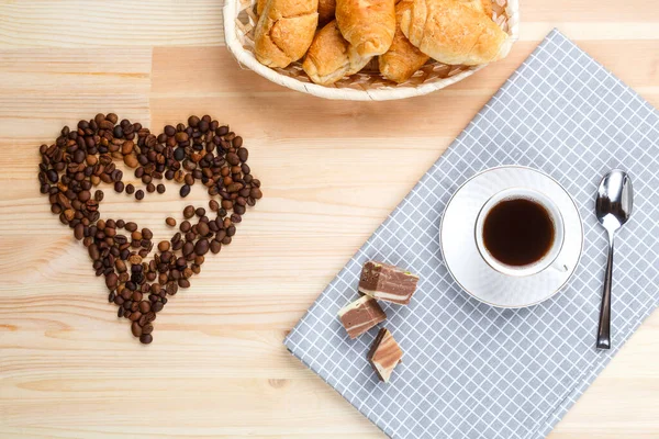 Una taza de café en una servilleta sobre una mesa de madera y una ictericia dispersa de café en forma de corazón . — Foto de Stock