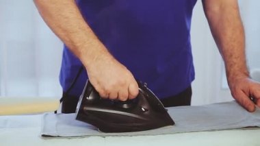 Bir adamın elindeki ütü ütü masasındaki giysileri ütülemektir.