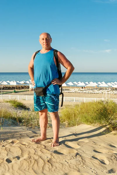 Un hombre en pantalones cortos y una camiseta en la playa sobre el fondo del mar . —  Fotos de Stock