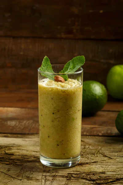Un bicchiere di frullato verde su un tavolo di legno sullo sfondo mela avocado lime . — Foto Stock