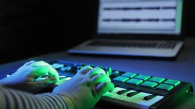 Kadın elleri bir MIDI klavyesinde çalıyor, dizüstü bilgisayar izlerken müzik kaydediyor