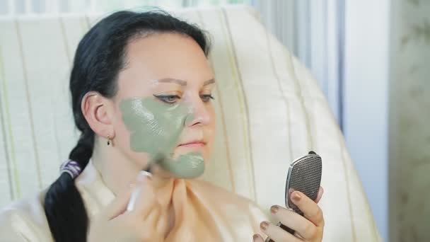 En kvinna hemma sätter en blå lermask på hennes ansikte.. — Stockvideo