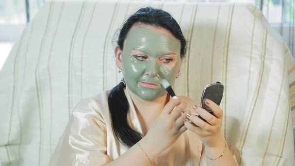Eine Frau zu Hause setzt sich eine Maske aus blauem Ton über das Gesicht. — Stockvideo
