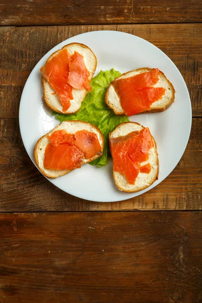 Bruschettas med lax och färskost på en vit platta på ett träbord. — Stockfoto