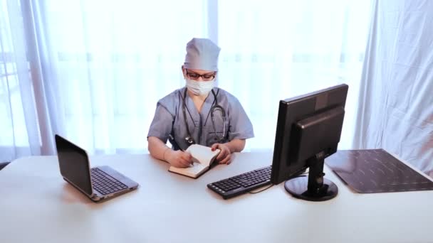 Una doctora en un consultorio con una máscara médica trabaja en una computadora . — Vídeo de stock